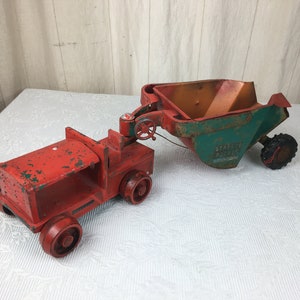 May include: Vintage red and green toy truck with a trailer. The truck has four red wheels and a red body with some paint wear. The trailer is green and orange with a black wheel and the text "Standard Roller" on the side.