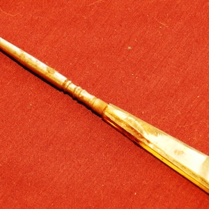 May include: A gold-toned shoe horn with a hook at one end and a pointed tip at the other. The handle is decorated with a pattern of lines.