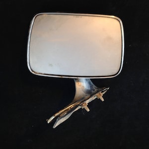 以下が含まれることがあります： 長方形でわずかに湾曲した鏡面を持つ、ヴィンテージカーのサイドミラー。 ミラーはクロムフレームで、取り付けボルト付きの金属ブラケットに取り付けられています。 クラシックカーの部品です。