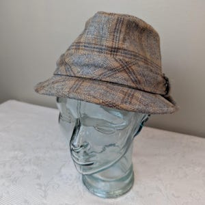 May include: A brown and blue plaid fedora hat with a brown leather band.