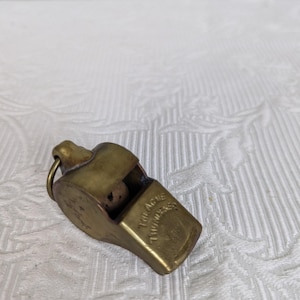 May include: A vintage brass whistle with a ring for attachment. The whistle has the text "THE ACME THUNDERER" engraved on the side. The whistle is a golden color and appears to be made of metal.