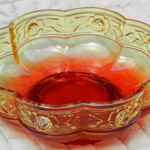 May include: A decorative, two-handled glass serving bowl with a scalloped edge. The bowl features a gradient of colors, transitioning from yellow to orange to red. Floral relief patterns adorn the rim and handles, adding a vintage touch to this kitchenware.
