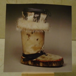 May include: A pair of fur-lined boots with a black leather strap and a brown fur cuff. The boots are made of a light brown fur with dark brown spots.
