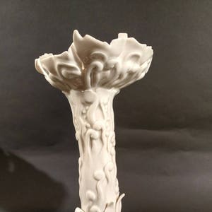 May include: A white ceramic candle holder with a floral design and a base shaped like a clawed foot.