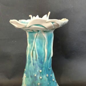 May include: A ceramic candle holder with a white top and a teal blue base. The base has a three-pronged design that resembles a foot.