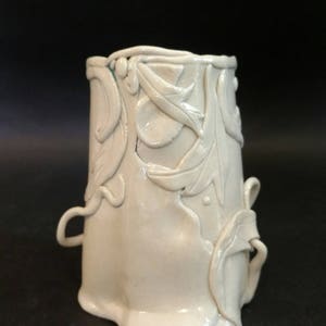 May include: A white ceramic vase with a textured, floral design. The vase has a unique, organic shape and a smooth, glossy finish.