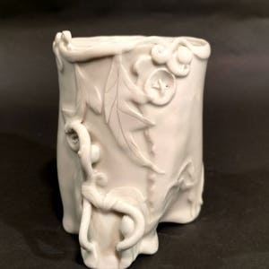 May include: White ceramic vase with a textured, organic design. The vase features raised floral and leaf motifs, creating a three-dimensional effect.
