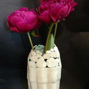 May include: A white ceramic vase with a textured, bubble-like design around the top. The vase is filled with three pink peonies.