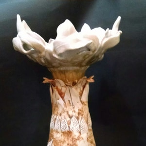 May include: A white ceramic vase with a flower-like top and a brown and white textured body. The vase has a unique design with leaves and a textured surface.