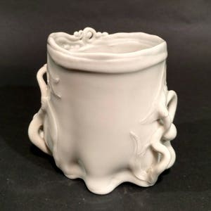 May include: A white ceramic vase with an ornate, flowing design. The vase has a wide, ruffled rim and sculpted floral and scrollwork details. The base has a wavy, irregular shape. The overall aesthetic is elegant and decorative.