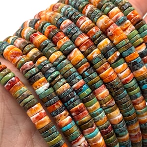 Puede incluir: Primer plano de hebras de cuentas de piedras preciosas de colores. Las cuentas son planas, en forma de disco, y presentan una variedad de colores, incluyendo naranja, turquesa, verde y marrón. Las cuentas están ensartadas, creando una apariencia texturizada y vibrante. Estas cuentas son adecuadas para la fabricación de joyas.