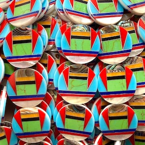 May include: A collection of circular inlay cabochons featuring a geometric pattern of light green, turquoise, red, yellow, black, and iridescent shell segments. Each piece is constructed from multiple small, flat, polished stone and shell sections.