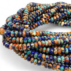 May include: Strands of colorful gemstone beads in shades of blue, orange, turquoise, and gold. The beads are oval-shaped and appear to be strung together, suitable for jewelry making or crafting projects.