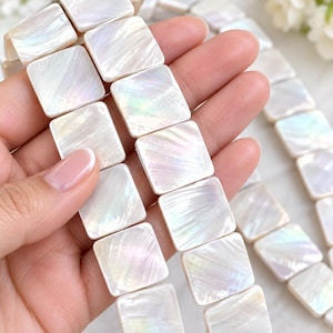 May include: A strand of square-shaped mother of pearl beads featuring a smooth, iridescent surface with a natural pearlescent sheen. Each bead displays a unique, subtle grain pattern with soft white and light rainbow reflections throughout the piece.