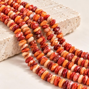 May include: Multiple strands of round, flat, disc-shaped beads in shades of orange, red, and cream. The beads feature a marbled, variegated texture with swirling patterns of deep crimson, bright orange, and soft white throughout each individual piece.