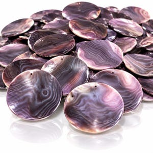 May include: A collection of circular, flat shell components featuring a polished, iridescent surface with swirling patterns in shades of deep purple, lavender, and white. Each piece has a small, singular hole drilled near the top edge for attachment.