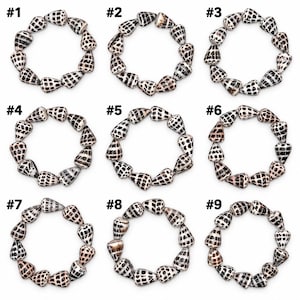 May include: Nine circular bracelets arranged in a grid, each numbered one through nine. Every bracelet is composed of individual cone-shaped seashells featuring a white base with black and brown geometric grid-like patterns.