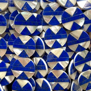 May include: A collection of circular buttons featuring a geometric inlay pattern. Each button is composed of alternating segments of iridescent white mother-of-pearl and deep blue lapis lazuli, separated by a horizontal blue bar across the center.