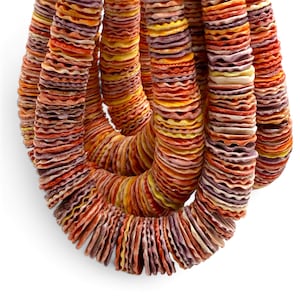 May include: A multi-strand necklace composed of numerous small, circular, ruffled shell beads in a vibrant gradient of orange, yellow, pink, and purple hues. The beads are strung together in dense, overlapping loops, creating a textured appearance.