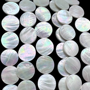 May include: A collection of circular mother of pearl buttons arranged in a grid pattern. Each button features a smooth, iridescent surface with swirling white, cream, and subtle rainbow-colored highlights, reflecting light against a black background.