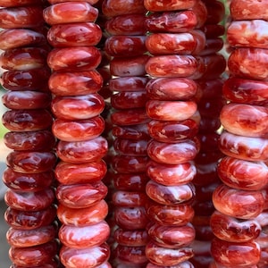 May include: Close-up of multiple strands of red and white banded gemstone beads. The beads are round and stacked, creating a textured, layered effect. The beads have a polished, glossy finish, and the color variation adds depth.
