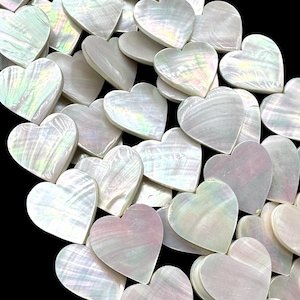 May include: A collection of heart-shaped pieces crafted from iridescent mother-of-pearl shell. Each piece features a smooth, polished surface with a natural pearlescent sheen that reflects subtle rainbow colors against a solid black background.
