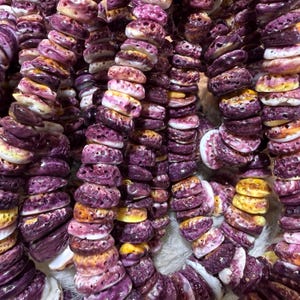 May include: A close-up of a strand of purple and yellow shell beads. The beads are irregular in shape and have a textured surface.