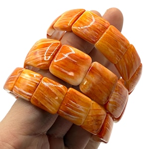 May include: A stretch bracelet composed of smooth, square-shaped beads in a vibrant orange and white marbled pattern. The beads feature a glossy, polished finish with visible light reflections, creating a cohesive, continuous band of orange stone-like segments.