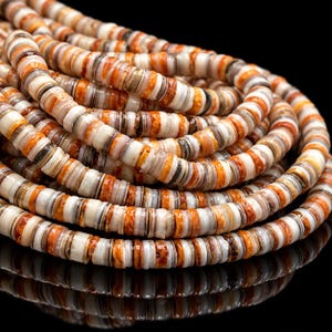 May include: A long strand of circular, flat disc-shaped beads arranged in a coiled formation. The beads feature a variegated pattern of white, cream, tan, and vibrant orange tones, with a smooth, polished finish and a consistent, uniform thickness.