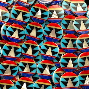 May include: A collection of circular inlay cabochons featuring a geometric pattern. Each piece displays a central white triangle, black triangular accents, light blue segments, a thin gold-tone band, and a vibrant red border on a blue base.