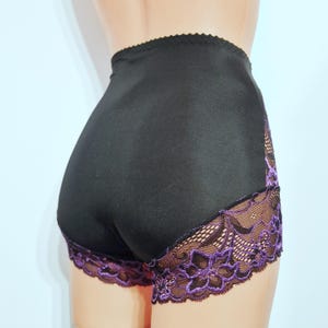 May include: Black high-waisted underwear with purple lace trim. The underwear has a smooth, opaque fabric with a scalloped edge at the waist. The lace trim features a floral design.