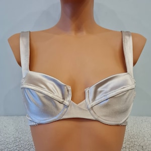 Könnte beinhalten: Ein Unterkleid aus Satin mit verstellbaren Trägern und einem tiefen Ausschnitt. Das Unterkleid ist hellbeige.