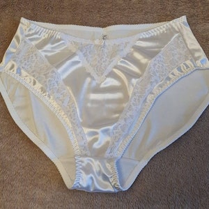 May include: White satin underwear with a lace trim. The underwear has a high leg cut and a low rise waist.