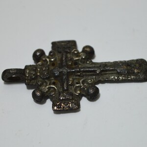 May include: A silver-toned metal cross pendant with intricate details and a loop for hanging. The cross has a raised center and is decorated with small, round accents.
