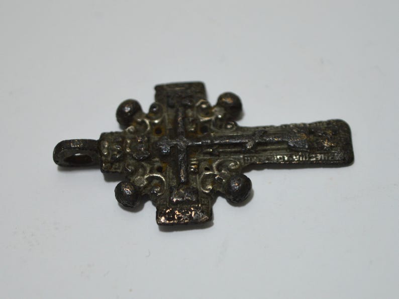 May include: A silver-toned metal cross pendant with intricate details and a loop for hanging. The cross has a raised center and is decorated with small, round accents.