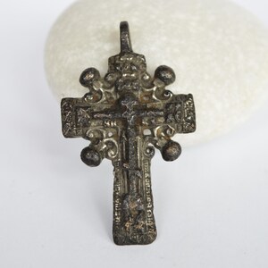 May include: An antique silver-toned cross pendant with intricate details and a figure of Jesus Christ on the front. The cross has a loop at the top for hanging.