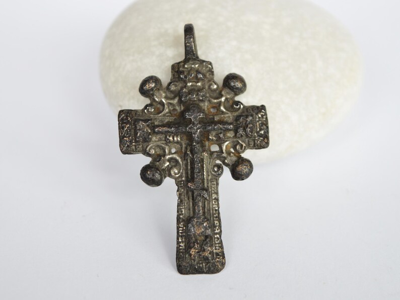 May include: An antique silver-toned cross pendant with intricate details and a figure of Jesus Christ on the front. The cross has a loop at the top for hanging.