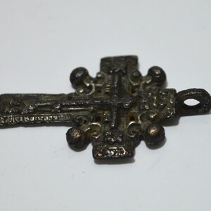 May include: A detailed, ornate, silver-toned metal cross pendant with a figure of Jesus Christ on the front. The cross has a loop at the top for hanging.