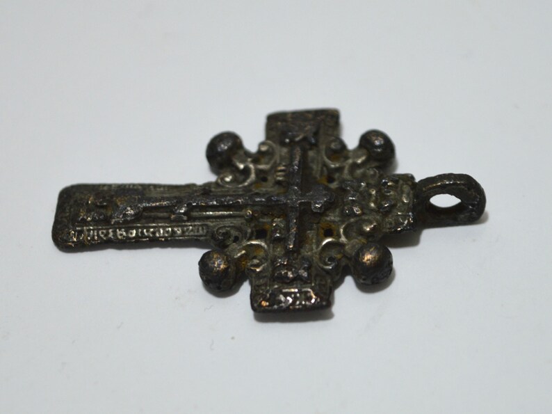 May include: A detailed, ornate, silver-toned metal cross pendant with a figure of Jesus Christ on the front. The cross has a loop at the top for hanging.