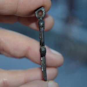 May include: A silver-toned metal pendant in the shape of a cross with a loop at the top. The cross has a decorative design with small round accents.