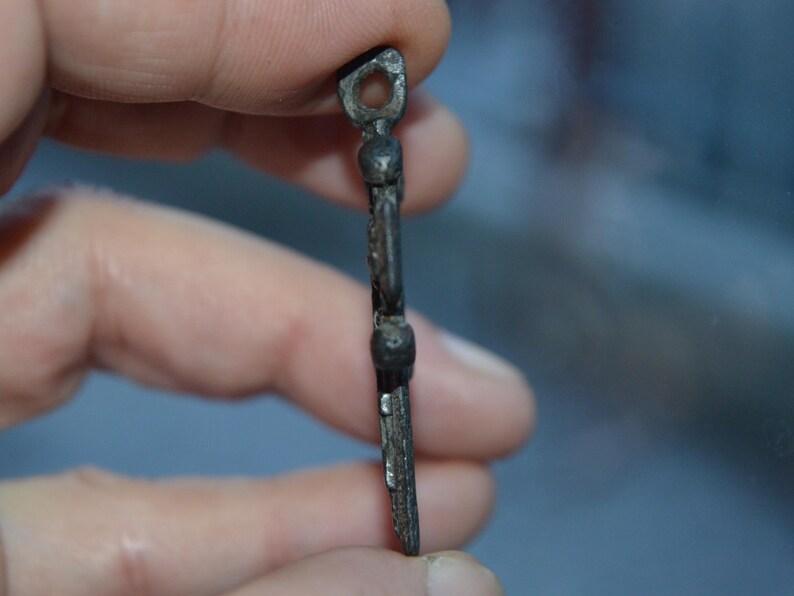 May include: A silver-toned metal pendant in the shape of a cross with a loop at the top. The cross has a decorative design with small round accents.