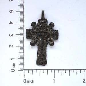 May include: A silver-colored, ornate cross pendant with a detailed design. The cross is approximately 3 cm in length and features a loop at the top for hanging.