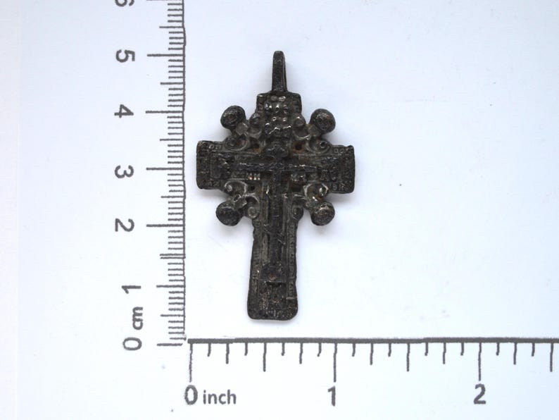 May include: A silver-colored, ornate cross pendant with a detailed design. The cross is approximately 3 cm in length and features a loop at the top for hanging.