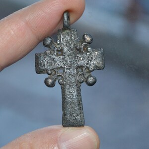 May include: A silver-toned cross pendant with intricate details and a loop at the top for hanging.