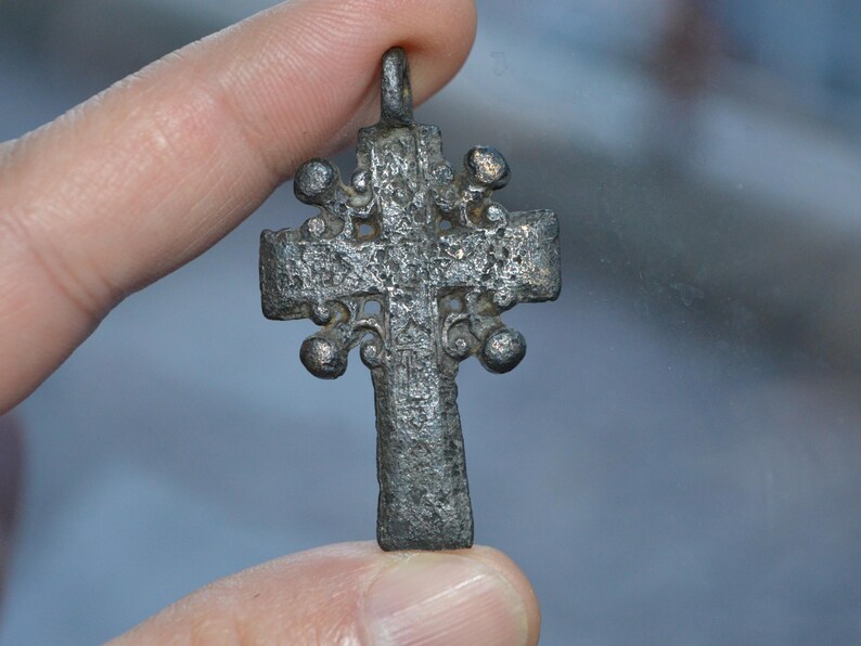 May include: A silver-toned cross pendant with intricate details and a loop at the top for hanging.