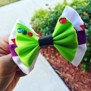 May include: A green, white, and purple bow with a black center and red, green, and blue rhinestones.