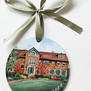 May include: A round, painted ornament depicting a brick building with a green lawn and red trees. The date "October 5, 2024" is written in white script at the bottom.