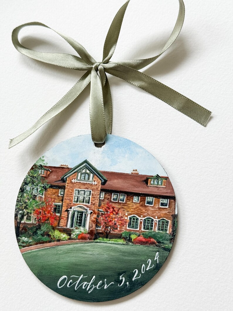 May include: A round, painted ornament depicting a brick building with a green lawn and red trees. The date "October 5, 2024" is written in white script at the bottom.