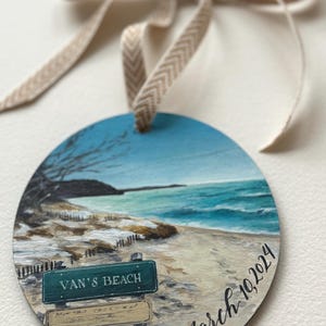 May include: A round wooden ornament featuring a painted scene of a beach with a sign that reads "Van's Beach" and the date "March 10, 2024".