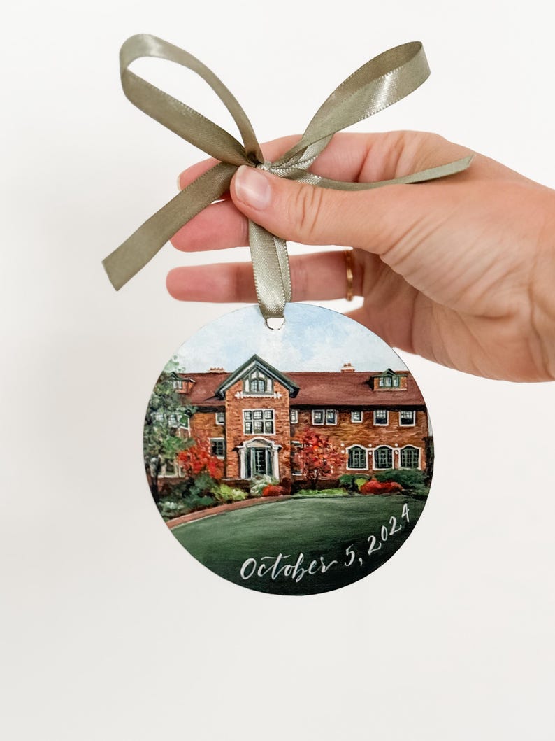 May include: A round, painted bauble depicting a brick building with a green lawn and trees. The bauble is decorated with the date "October 5, 2024" in white calligraphy.